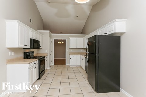 A black refrigerator in a kitchen with white cabinets.