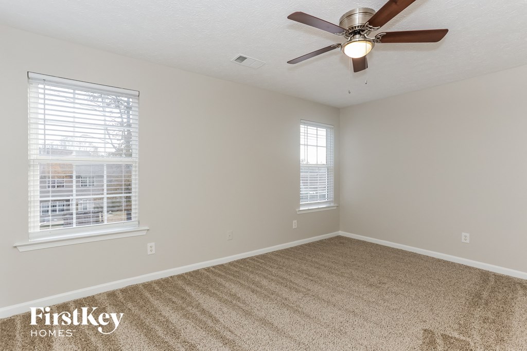 an empty room with a ceiling fan and two windows
