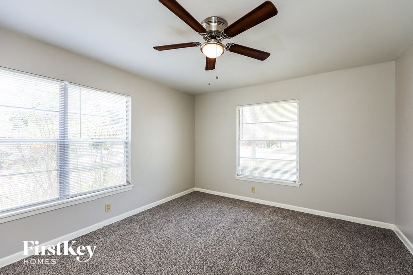 an empty room with a ceiling fan and two windows