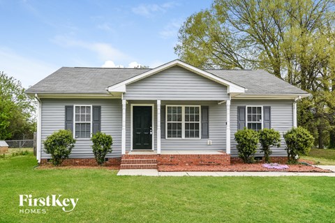 A grey house with a black door and windows is surrounded by a green lawn.