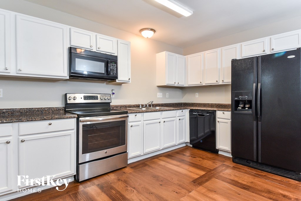 A kitchen with white cabinets and a black refrigerator.