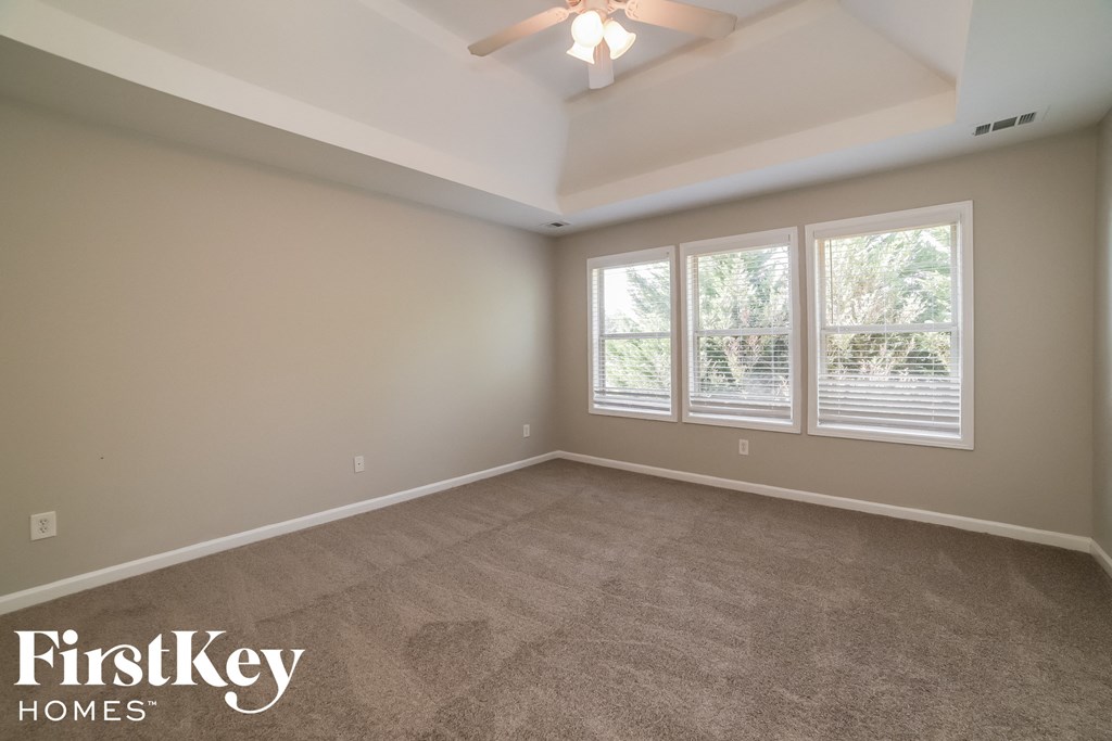 a empty living room with a ceiling fan and three windows