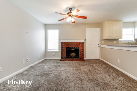 an empty living room with a brick fireplace and a ceiling fan