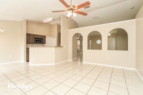 A spacious living room with a kitchen in the background and a fan on the ceiling.