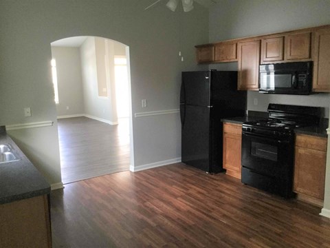 an empty kitchen with black appliances and wooden floors