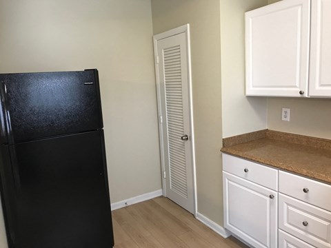 A black fridge sits in a kitchen with white cabinets and a brown counter.