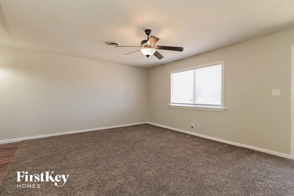 A room with a carpeted floor, a ceiling fan, and a window.