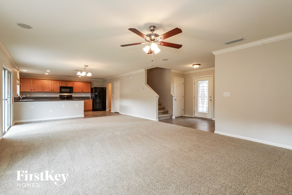 an empty living room with a ceiling fan and a kitchen