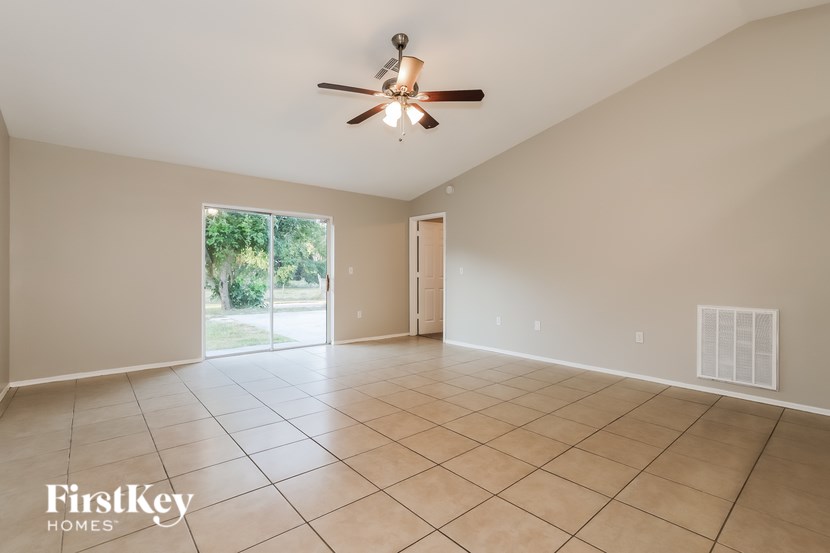 A spacious room with a ceiling fan and a sliding glass door leading to a garden.