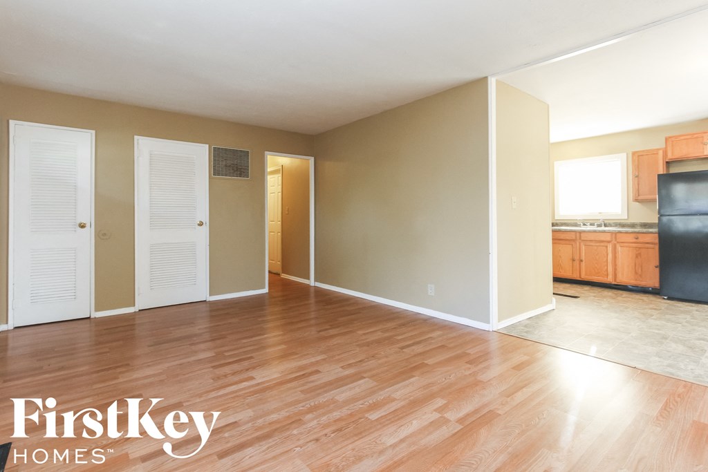 A room with wooden floors and a kitchen area in the background.
