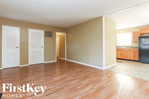 A room with wooden floors and a kitchen area in the background.