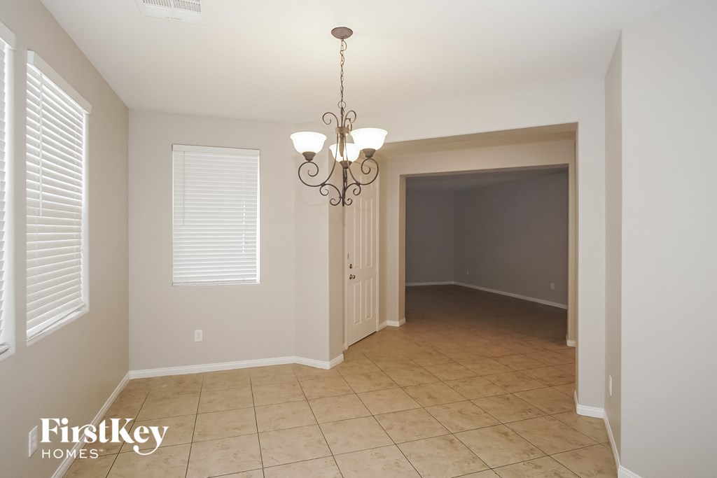 an empty dining room with a chandelier and a door to the kitchen