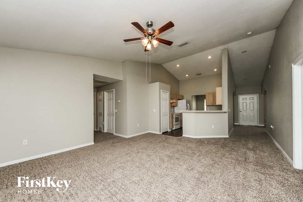 a spacious living room with carpet and a ceiling fan