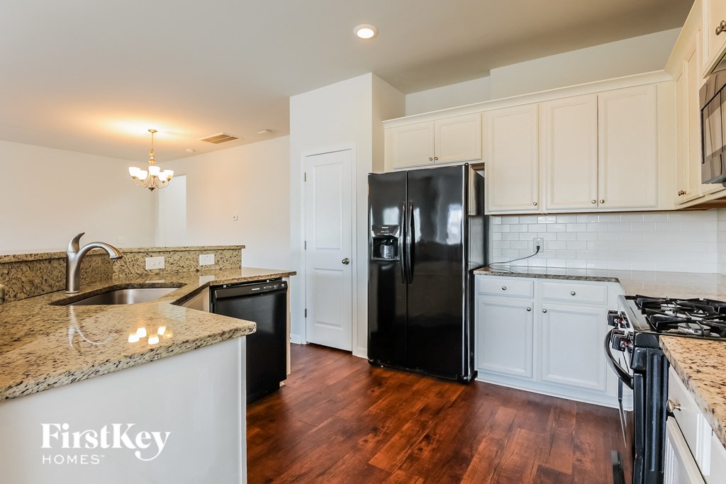 A kitchen with a black refrigerator and wooden floors.