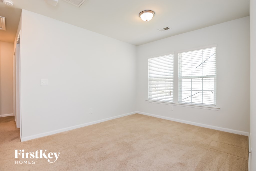 A room with a carpeted floor, a window with blinds, and a light fixture on the ceiling.
