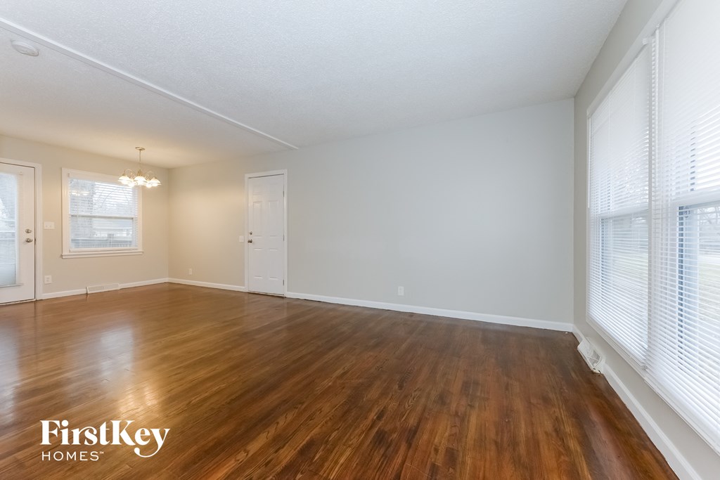 A room with wooden floors and white walls, with a window on the right side.