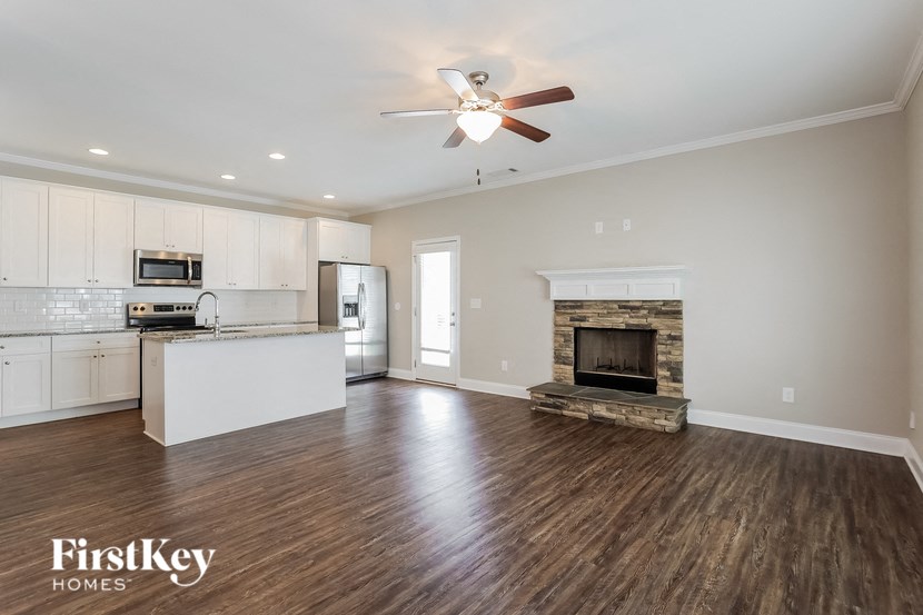A spacious living room with a fireplace and a kitchen area in the background.