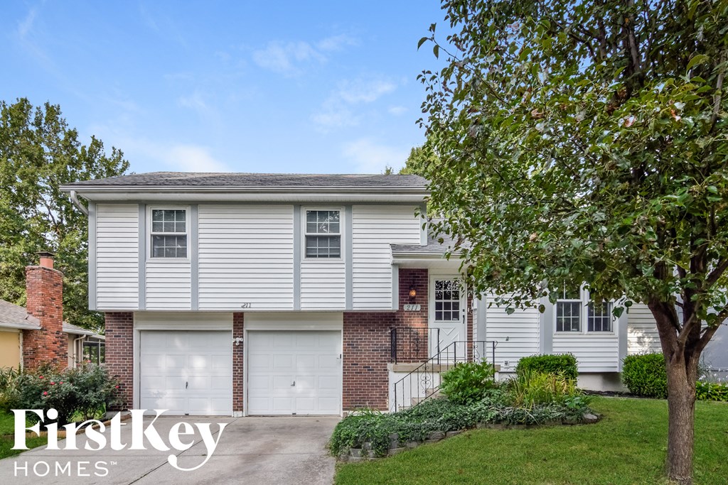 A house with a garage and a tree in front of it.