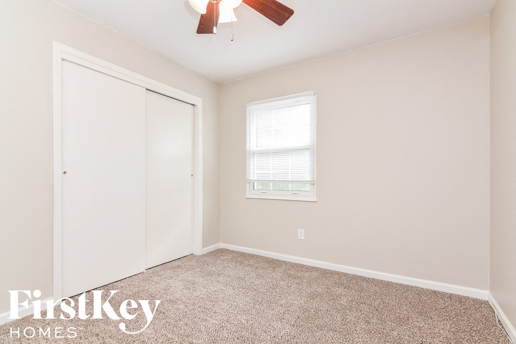 A room with a carpet floor, a ceiling fan, and a window with blinds.