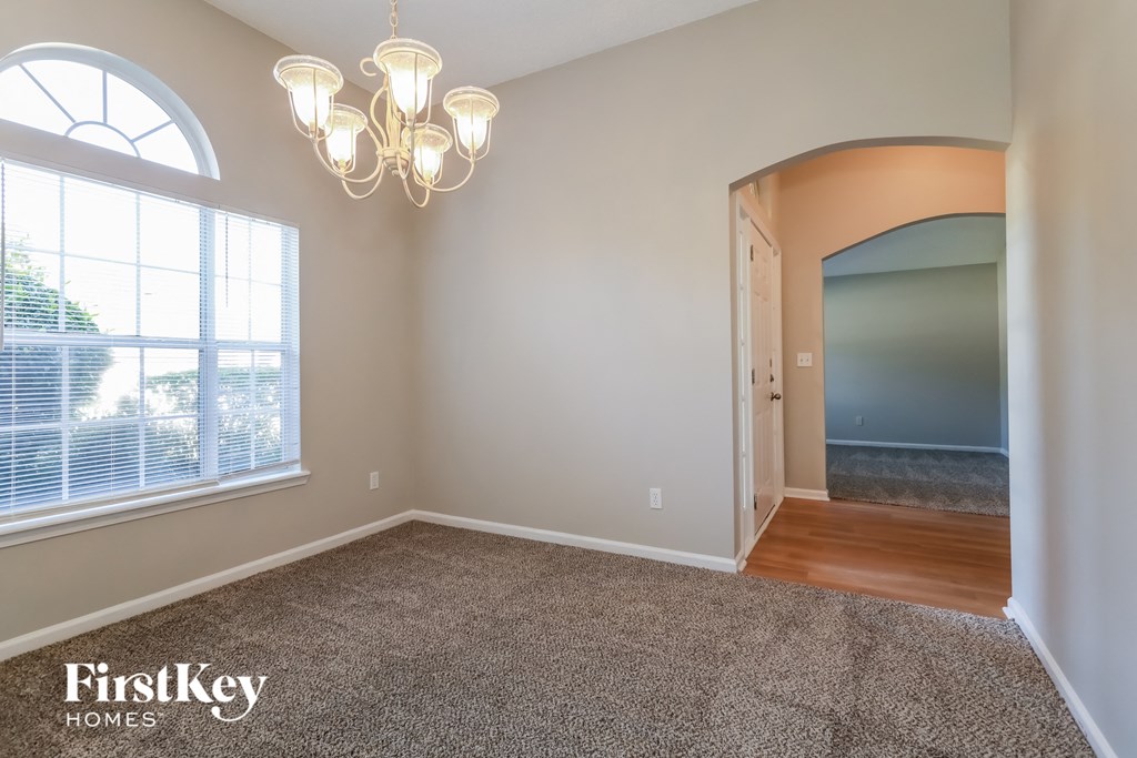 an empty dining room with a large window and a chandelier