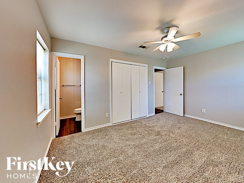 A carpeted room with a ceiling fan and a window with blinds.