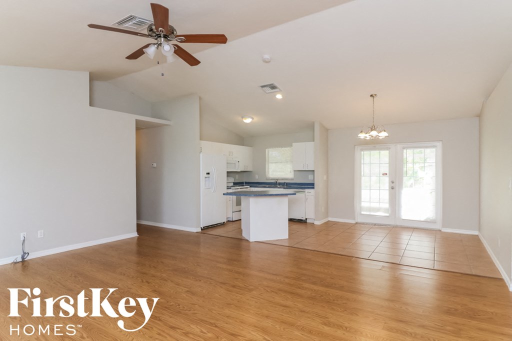 an empty living room and kitchen with wood floors and a ceiling fan