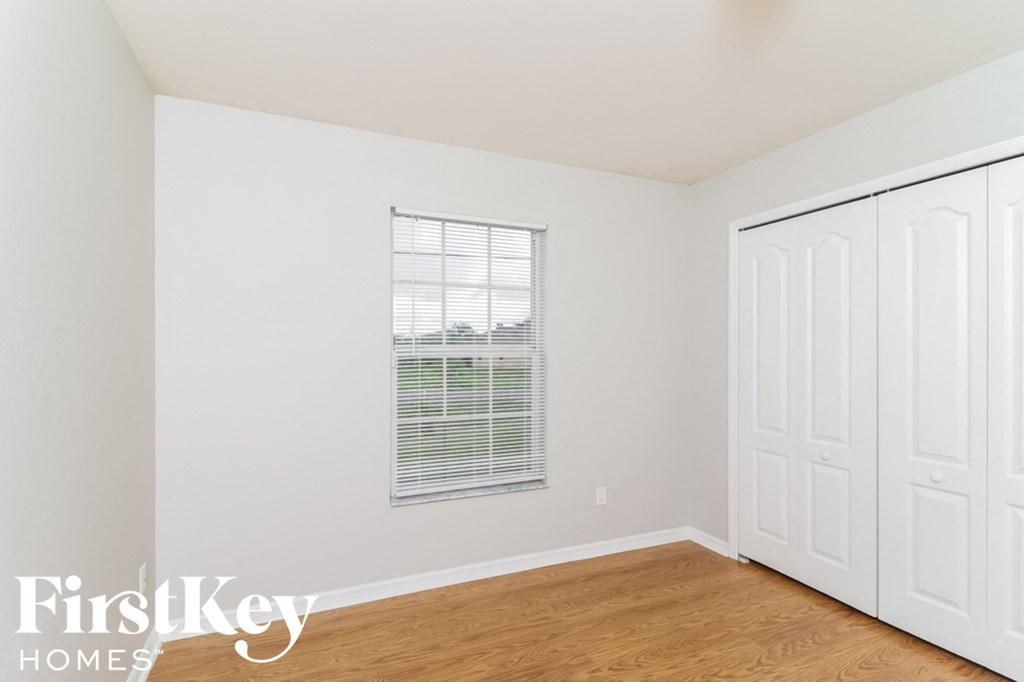 a bedroom with white walls and wood floors and a window