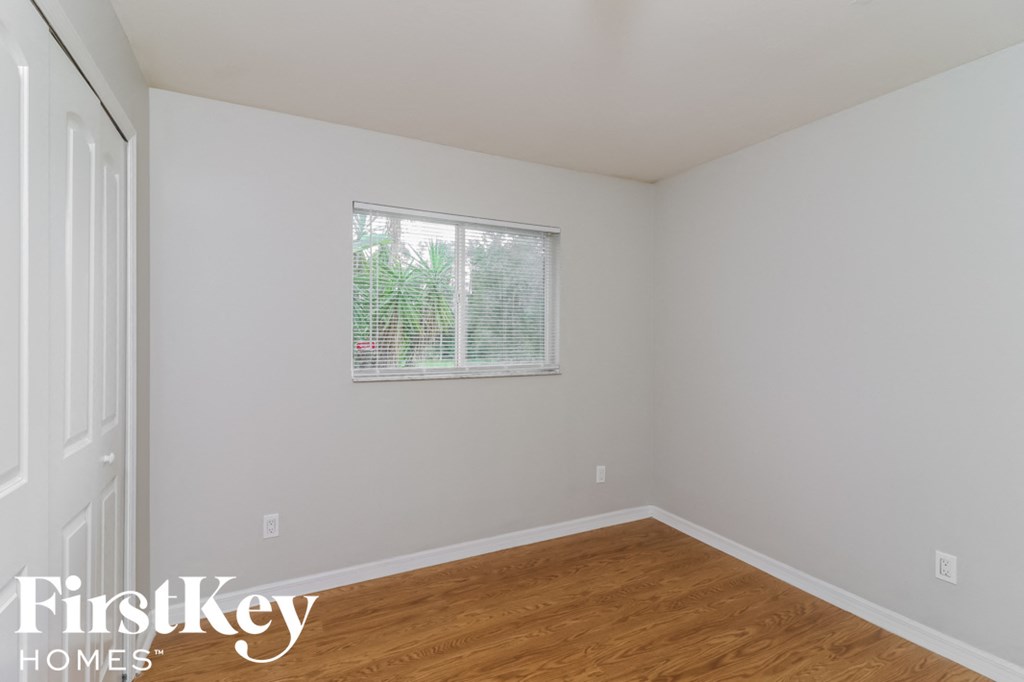 a bedroom with white walls and a window and wood floors