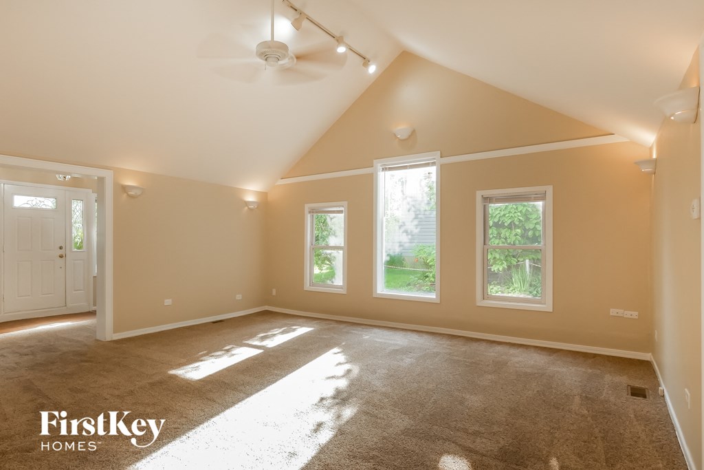 an empty living room with a ceiling fan and three windows