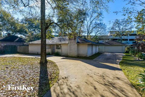 A house with a driveway and a tree in the foreground.