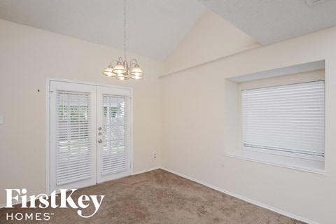 A room with a carpeted floor, a window with blinds, a door with a window, and a light fixture hanging from the ceiling.
