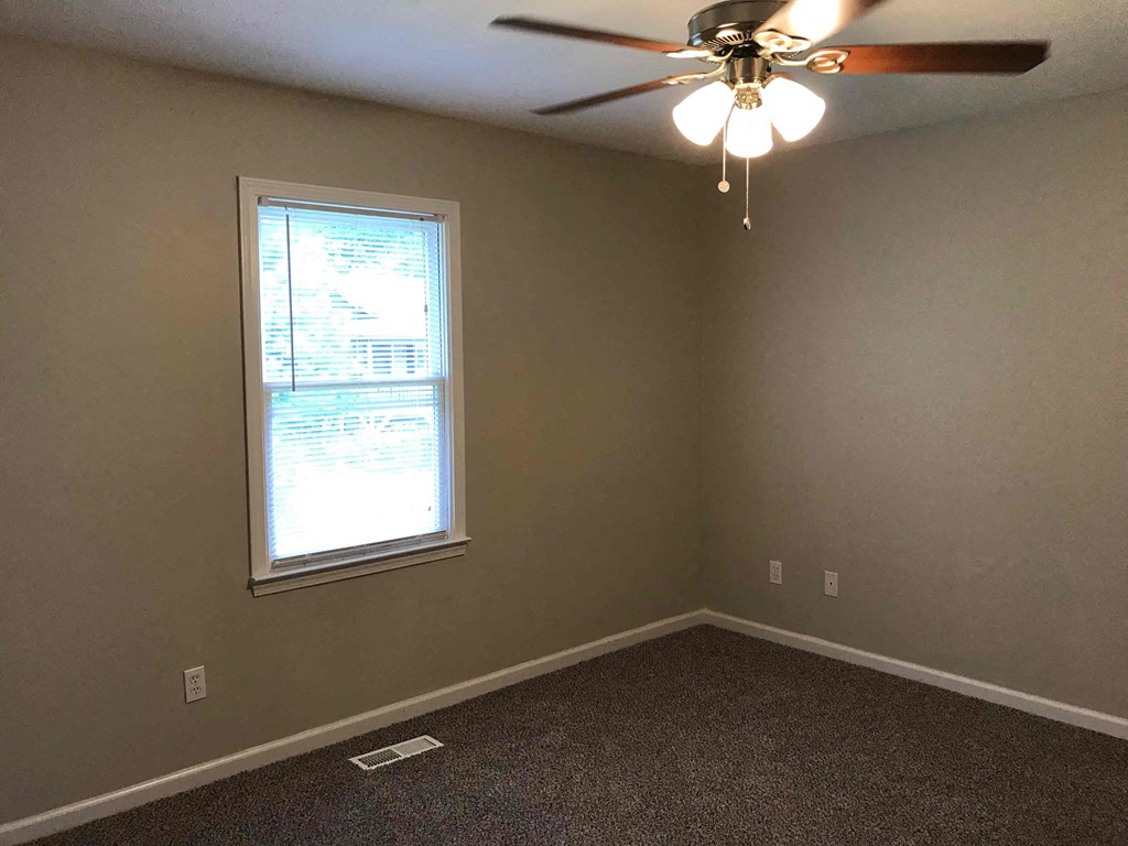 an empty bedroom with a ceiling fan and a window