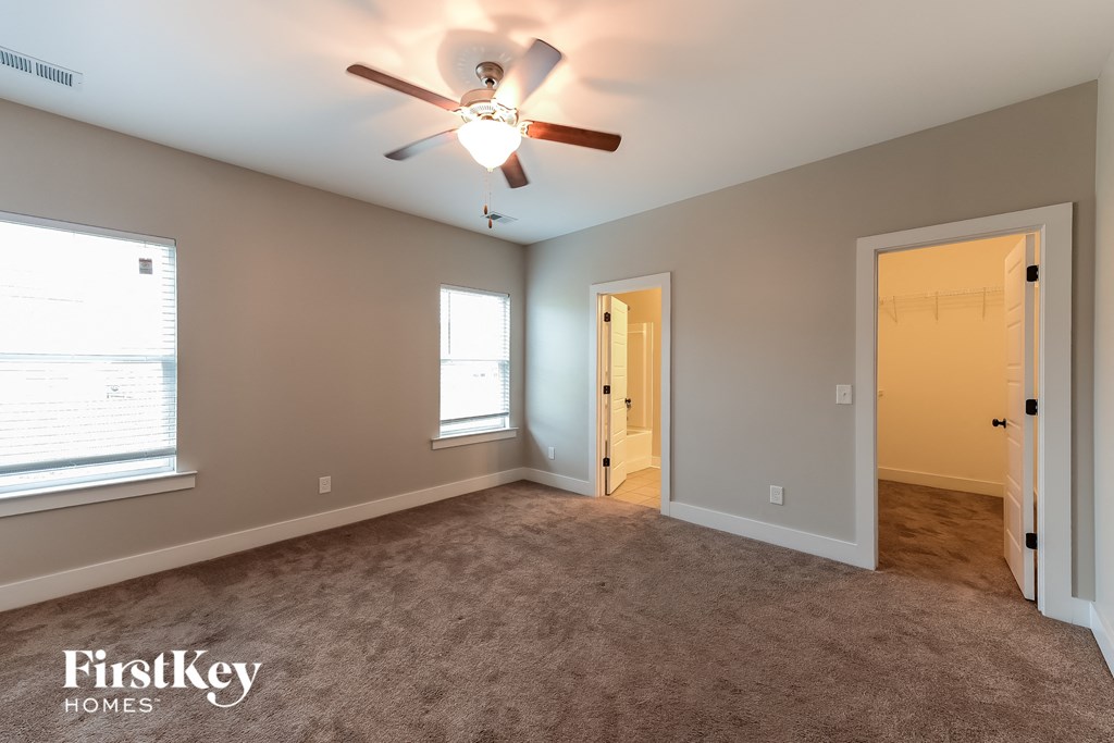 an empty living room with a ceiling fan and a door to a hallway