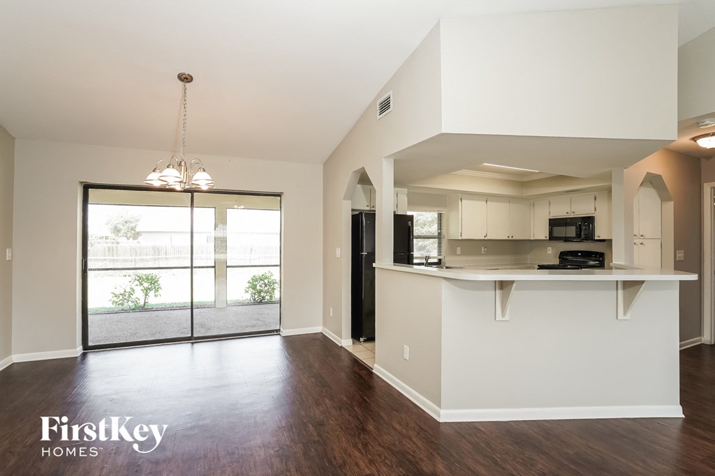 an empty living room with a kitchen and a door to a balcony