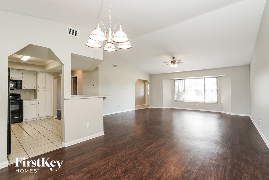 an empty living room and kitchen with wood flooring and a ceiling fan