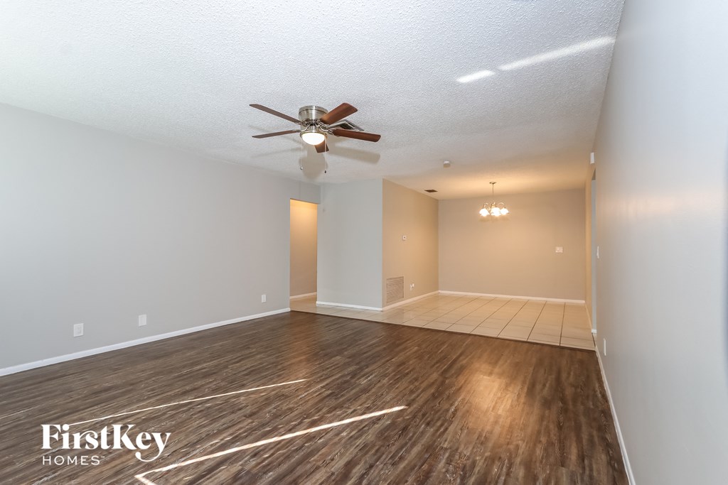 the spacious living room with hardwood flooring and a ceiling fan