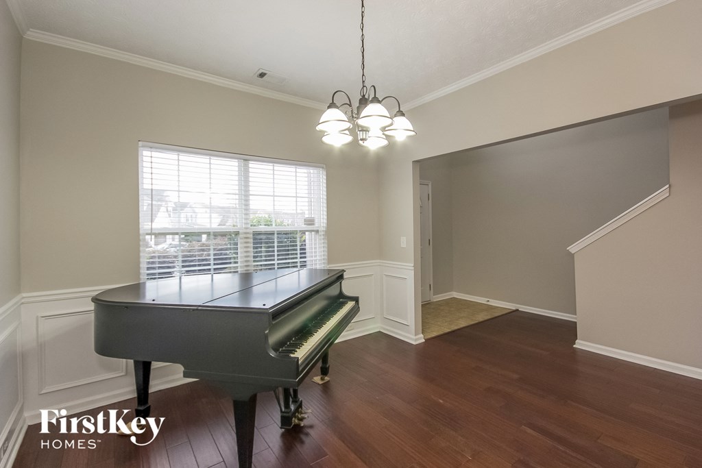 A grand piano sits in a room with wood floors and a chandelier.