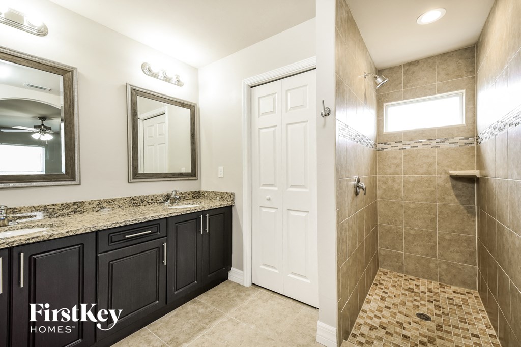 the master bathroom has a large walk in shower and a double vanity with black cabinets