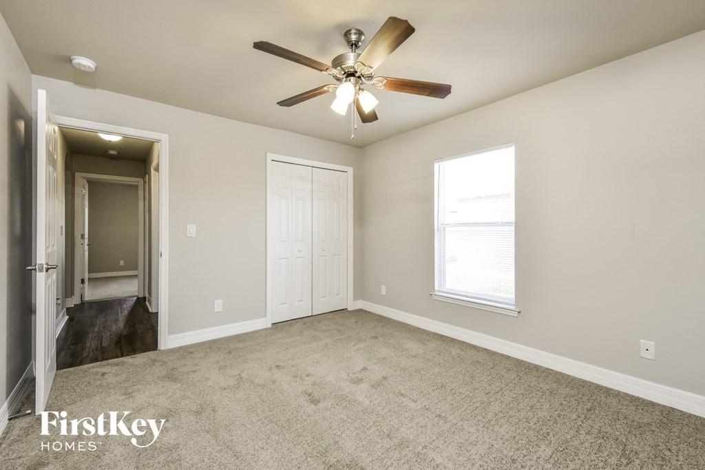 an empty living room with a ceiling fan and a door to a hallway