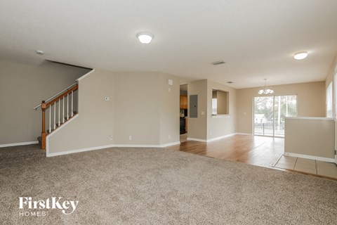 A spacious living room with a carpeted floor and a staircase on the left side.