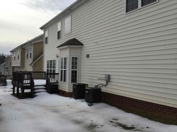 A house with a white siding and a black trash can in front of it.