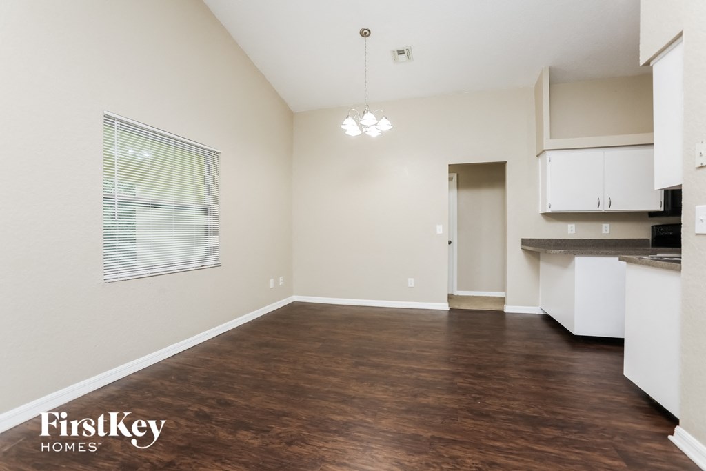 A room with wooden flooring and a kitchen area in the background.
