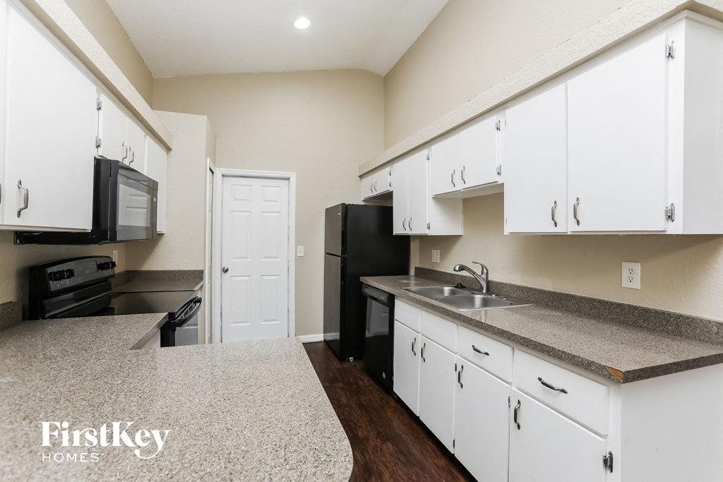 A kitchen with white cabinets and a black fridge.