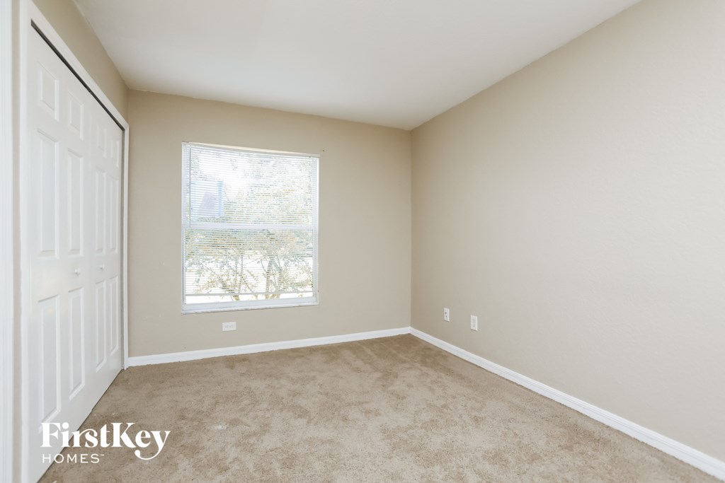 A room with a white door and a window with a view of trees.
