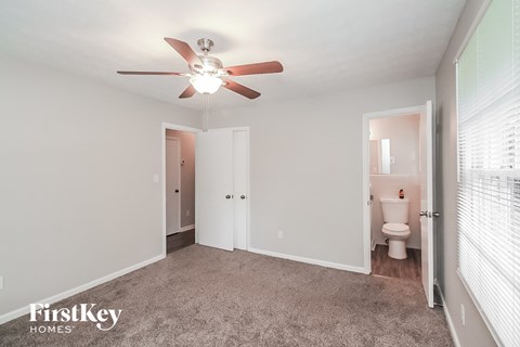 A bedroom with a fan and a toilet in the other room.