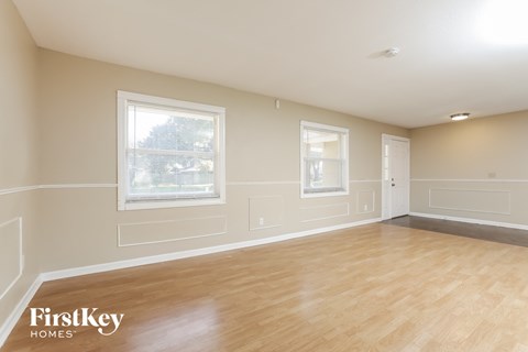 A spacious room with wooden floors and two windows.