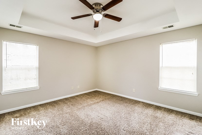 A room with a ceiling fan and two windows.