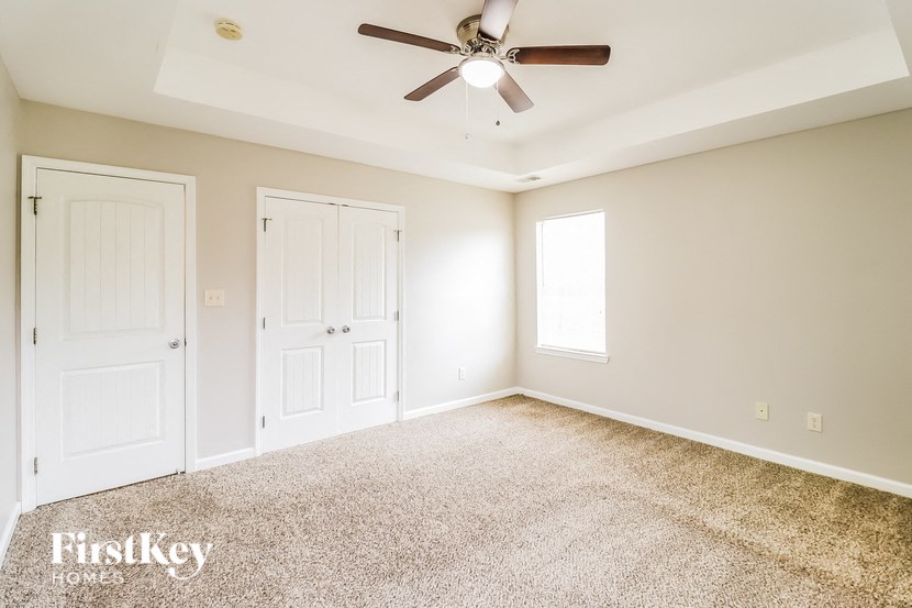 A spacious room with a carpeted floor, a ceiling fan, and two doors.