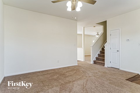A spacious room with a carpeted floor and a staircase in the background.