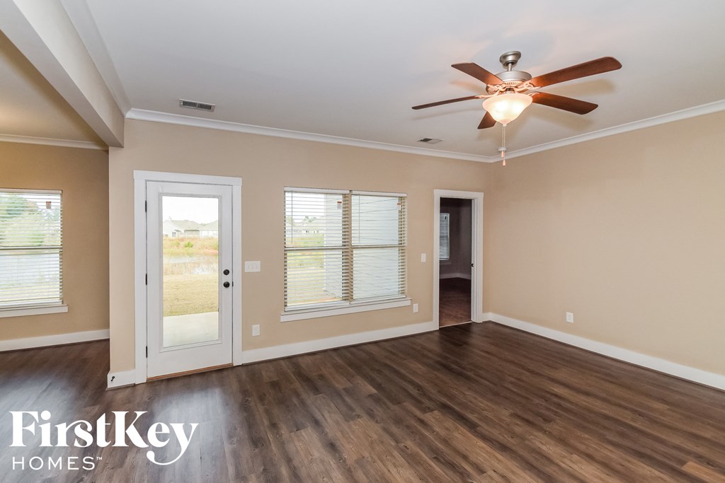 the living room of an empty house with a ceiling fan and a door to a